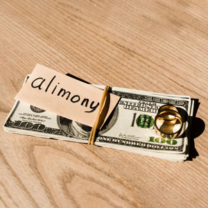 Money and wedding rings on a wooden table, with the word "alimony," symbolizing alimony & spousal maintenance.